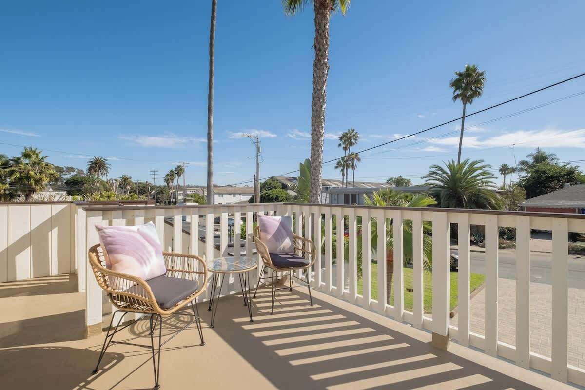 A balcony with two wicker chairs and a small table, surrounded by a white railing.