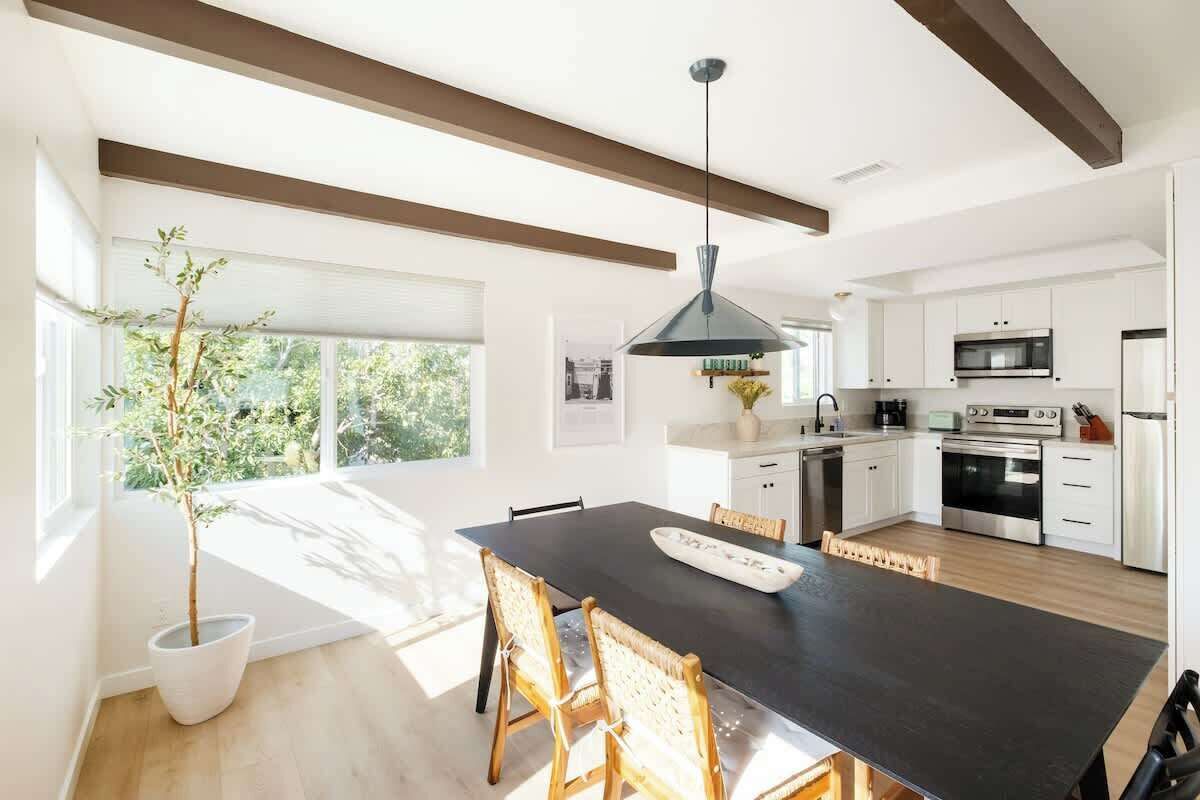 A modern kitchen with white cabinets, a black countertop, and stainless steel appliances. There is a dining table with chairs in the center of the room.