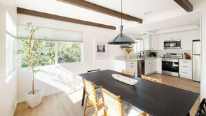 Une cuisine moderne avec des meubles blancs, un plan de travail noir et des appareils en acier inoxydable. Au centre de la pièce, on trouve une table à manger entourée de chaises.