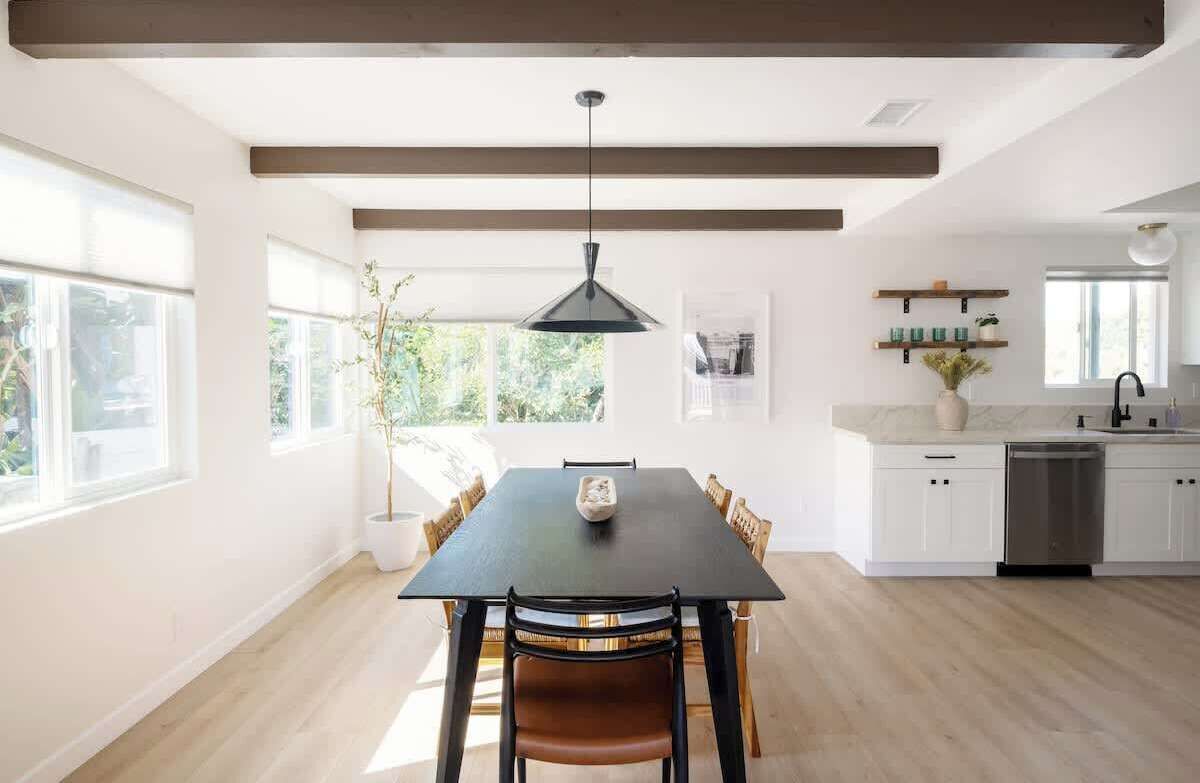 A modern kitchen with white cabinets, a black dining table, and a pendant light.