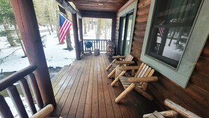 Een houten terras met een overdekte veranda, een barbecue en een vlag.