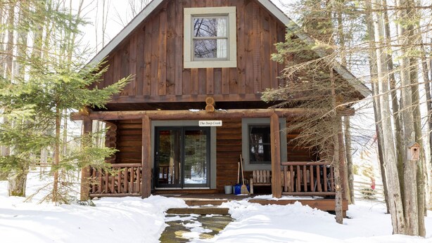 Een houten hut met een veranda, een groot raam en een bordje met de tekst 'The Deep Creek'.