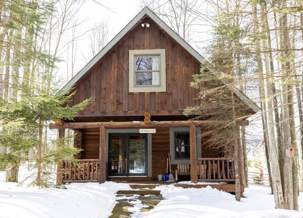 A wooden cabin with a front porch, a large window, and a sign reading "The Deep Creek".