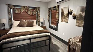 Un dormitorio con cama, ventilador de techo, aire acondicionado y mesita de noche con lámpara.