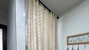 Un baño con cortina de ducha color beige, espejo con marco de madera y toallas a rayas colgadas en la pared.