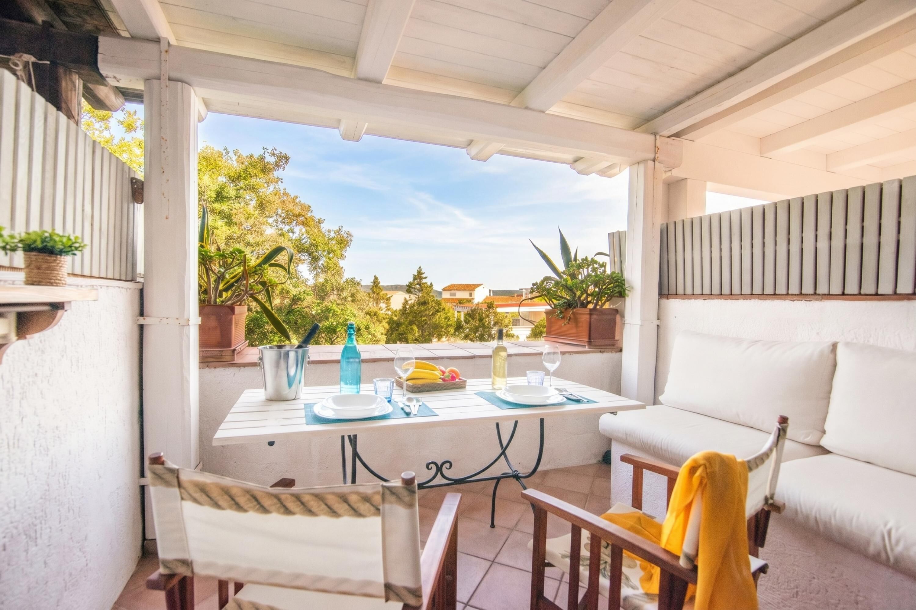 A covered patio with a table set for dining, a sofa, and potted plants.