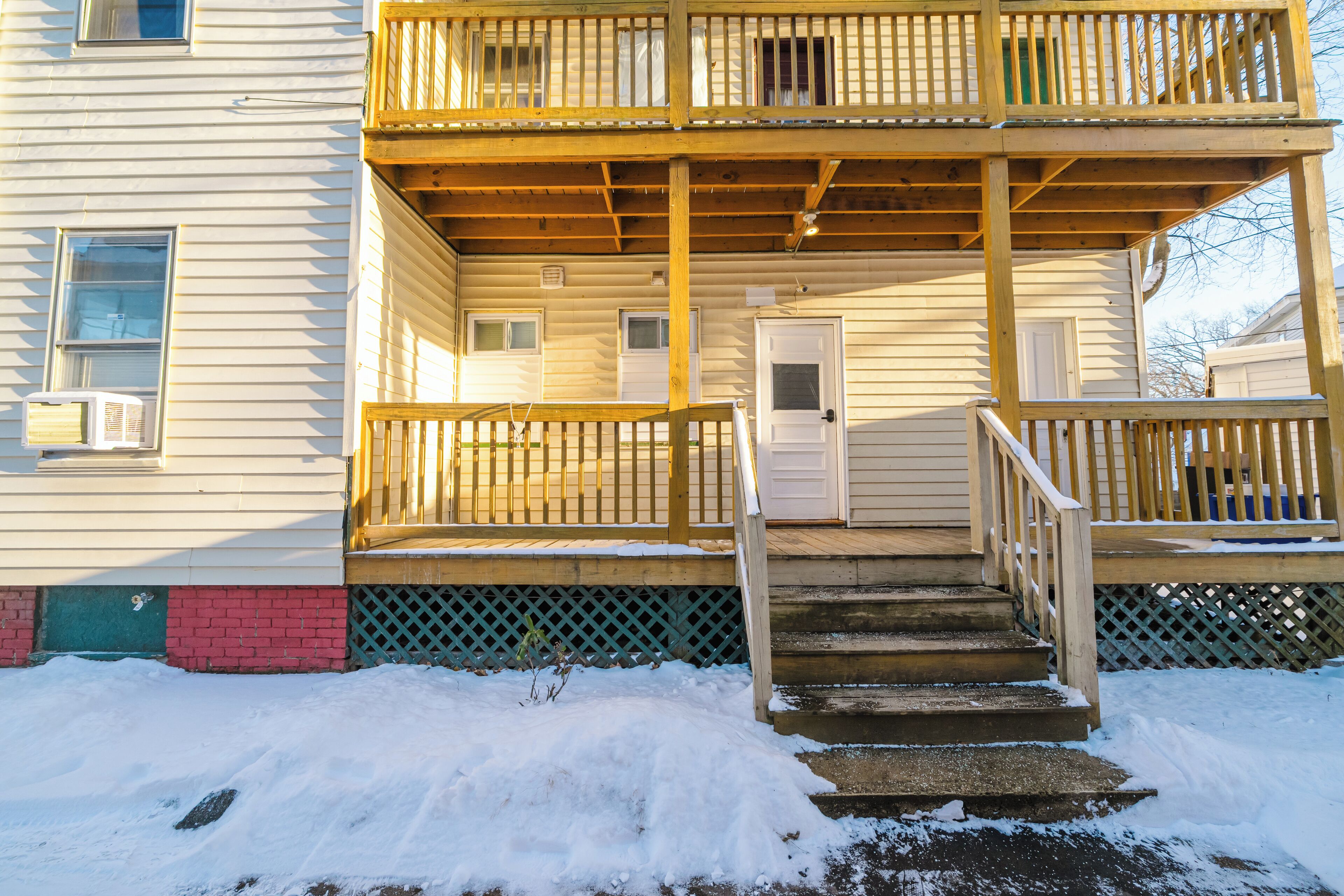 Un bâtiment à deux étages doté d’une terrasse en bois et d’un escalier menant à l’entrée.