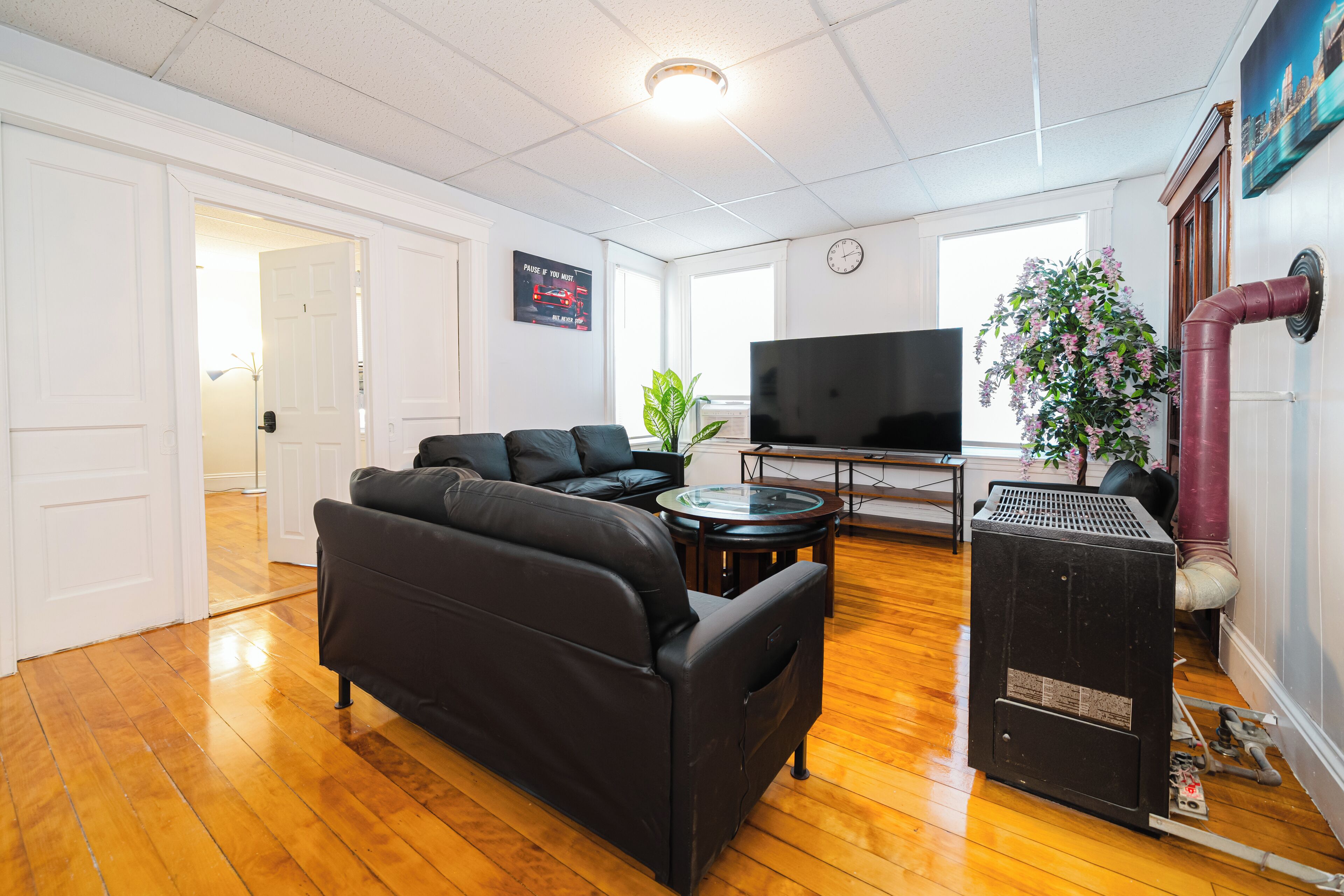 A living room with a black leather sofa, a flat-screen TV, a round coffee table, and a potted plant.