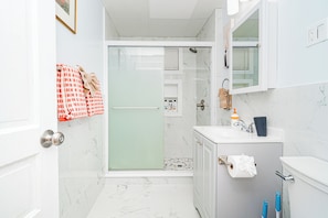 Een moderne badkamer met een douchecabine van glas, een wit wastafelmeubel met spiegel en een marmeren vloer.