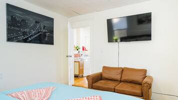 Um quarto com uma cama, um sofá de couro marrom, uma televisão de tela plana e uma pintura com vista para a cidade na parede.