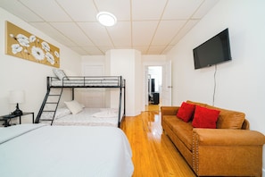 Een kamer met stapelbedden, een slaapbank, een televisie en een schilderij.