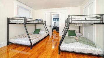 A room with two bunk beds, wooden flooring, a door leading to another room, and a window with blinds.