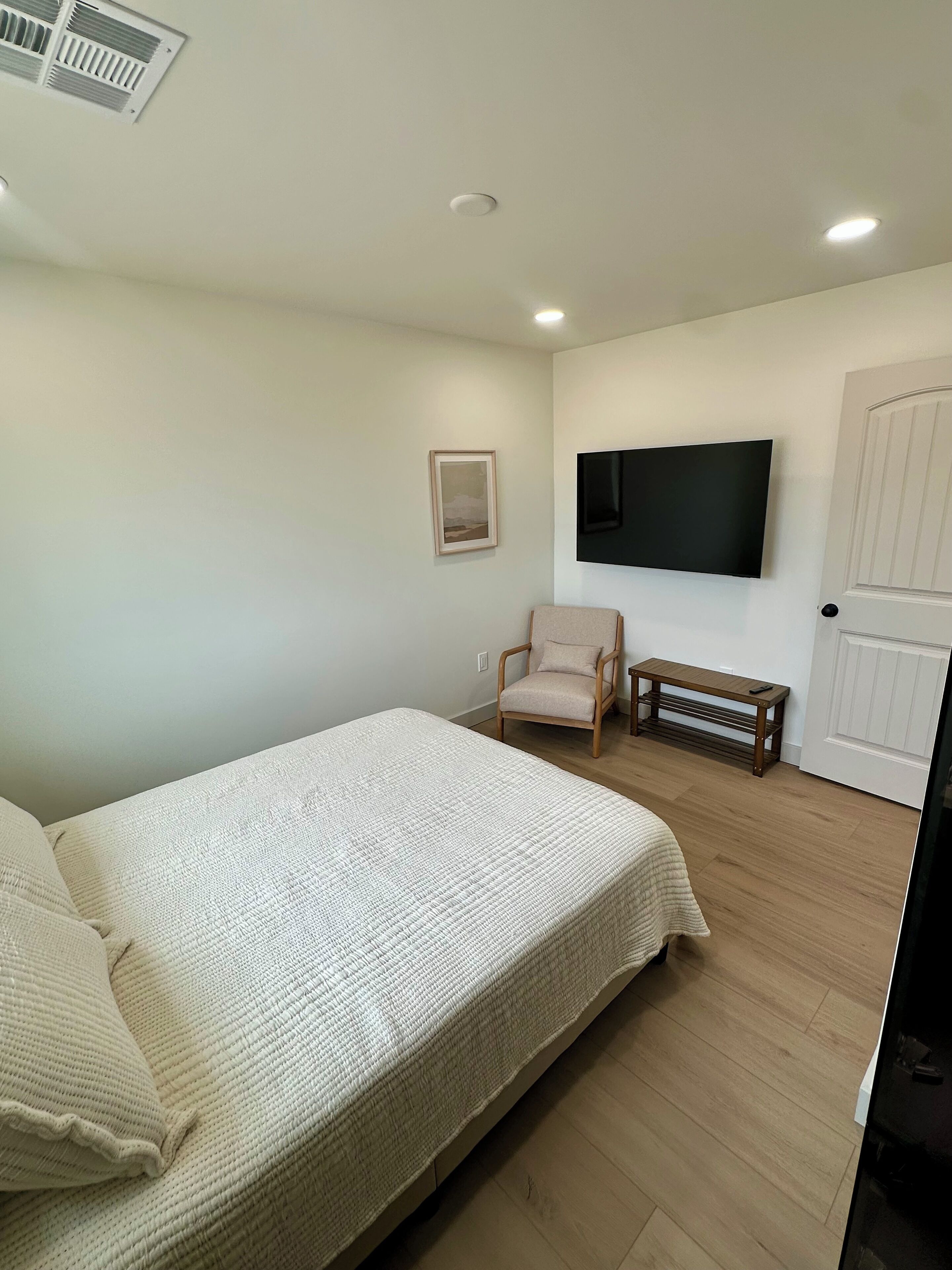 A bedroom with a bed, a chair, a TV, and a door.