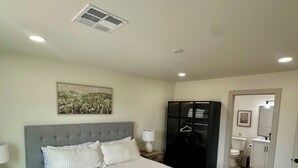 Une chambre à coucher avec un grand lit, une table de chevet avec une lampe, une armoire et une salle de bain visible à travers une porte ouverte.