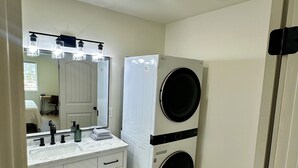 Une buanderie avec des lave-linge et des sèche-linge superposés, un évier avec un miroir et un tapis à motifs.