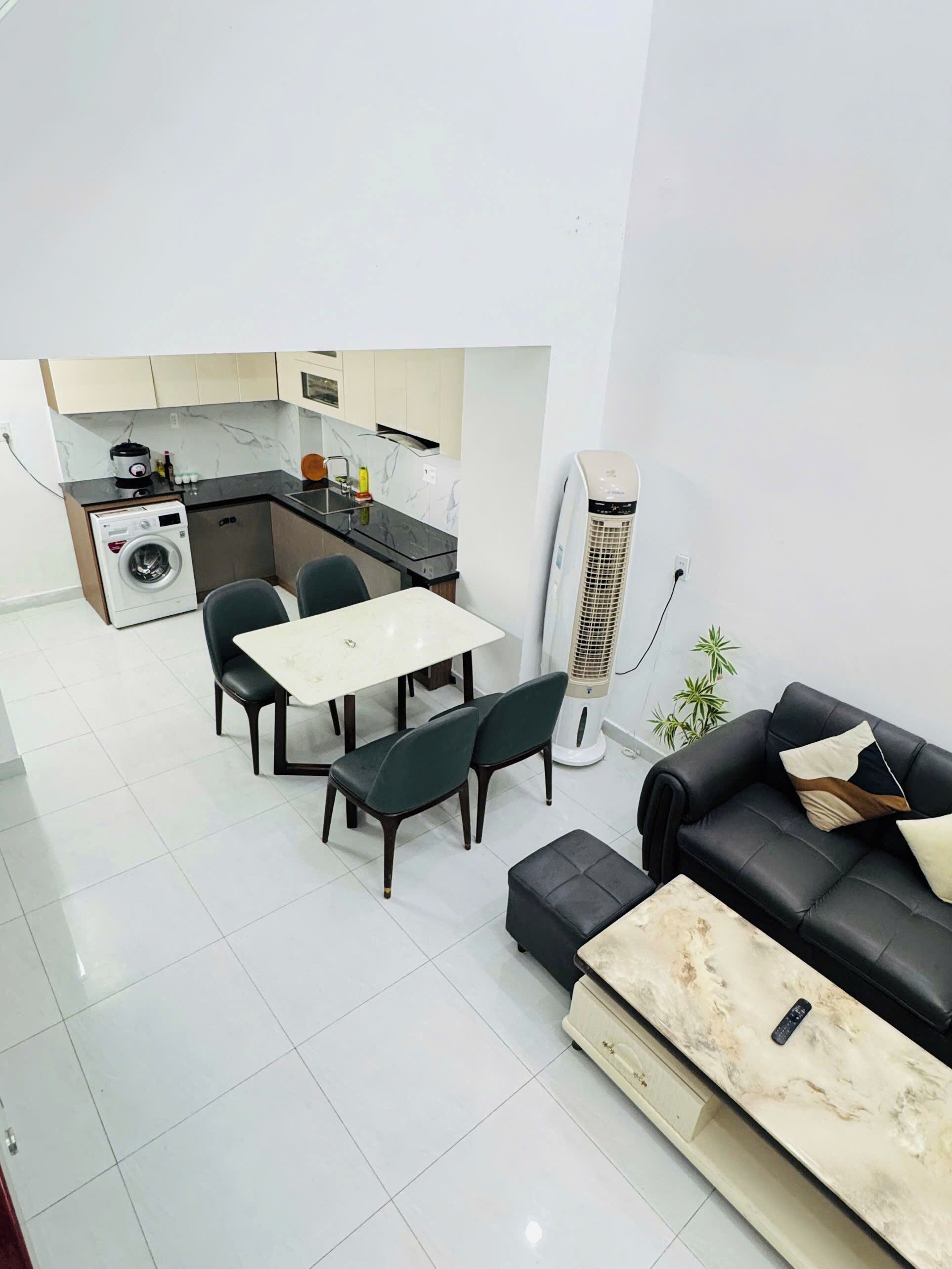 A modern living room with a black leather sofa, a marble coffee table, and a dining area with a white table and dark chairs.