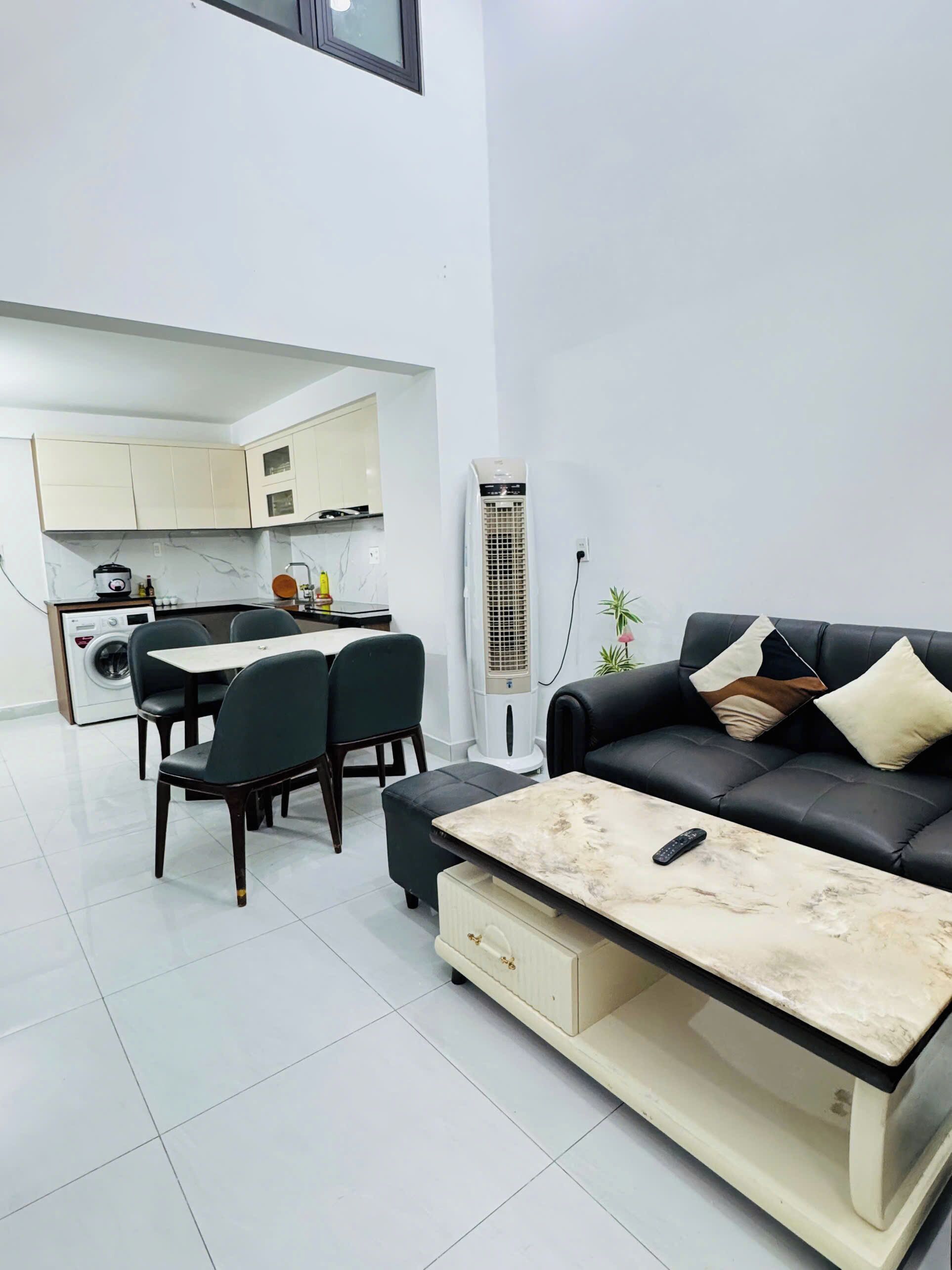 Uma sala de estar moderna com um sofá de couro preto, uma mesa de centro de mármore e um espaço de jantar com mesa e cadeiras.