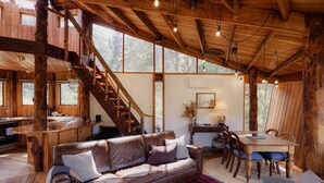 Interior rústico de uma cabana com escada de madeira, sofá de couro, mesa de jantar e área de cozinha.