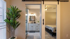 A bedroom with a bed, a sliding door leading to a bathroom with a mirror, and a potted plant. - Suburban Retreat Central to Dallas, Plano & Frisco (Dallas)