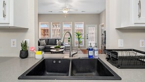 A kitchen with a double sink, a ceiling fan, and a view into the living area. - Suburban Retreat Central to Dallas, Plano & Frisco (Dallas)