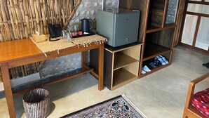 Una habitación pequeña con una mesa de madera, un televisor, un tapete tejido, una cafetera y un zapatero.