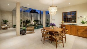 Amplo espaço interno com piscina, mesa de jantar com cadeiras, lustre e cozinha.