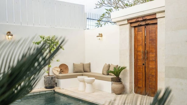 Uma área à beira da piscina com um espaço de estar integrado, uma porta de madeira e plantas em vasos.