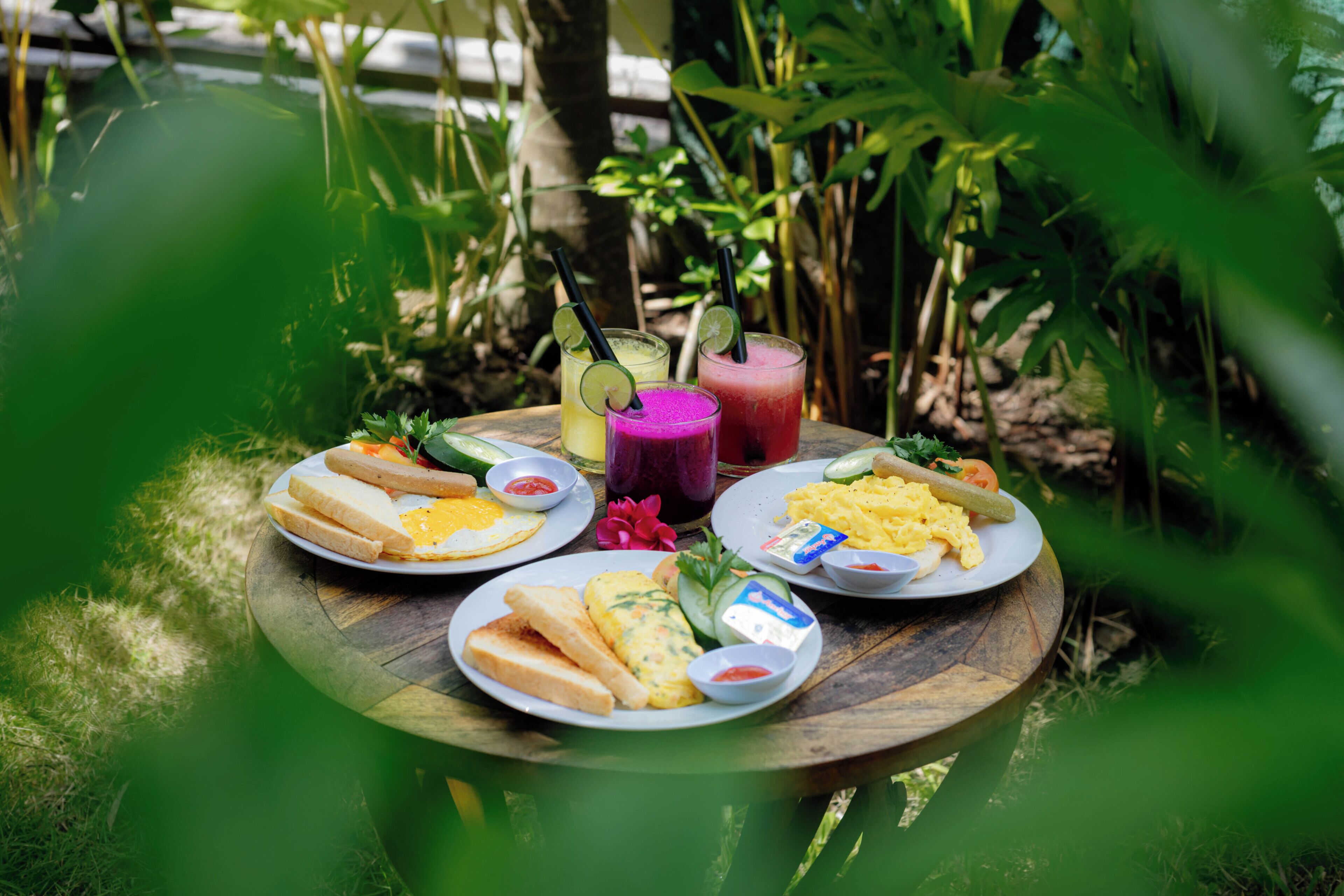 A round wooden table with plates of food and drinks, surrounded by greenery.