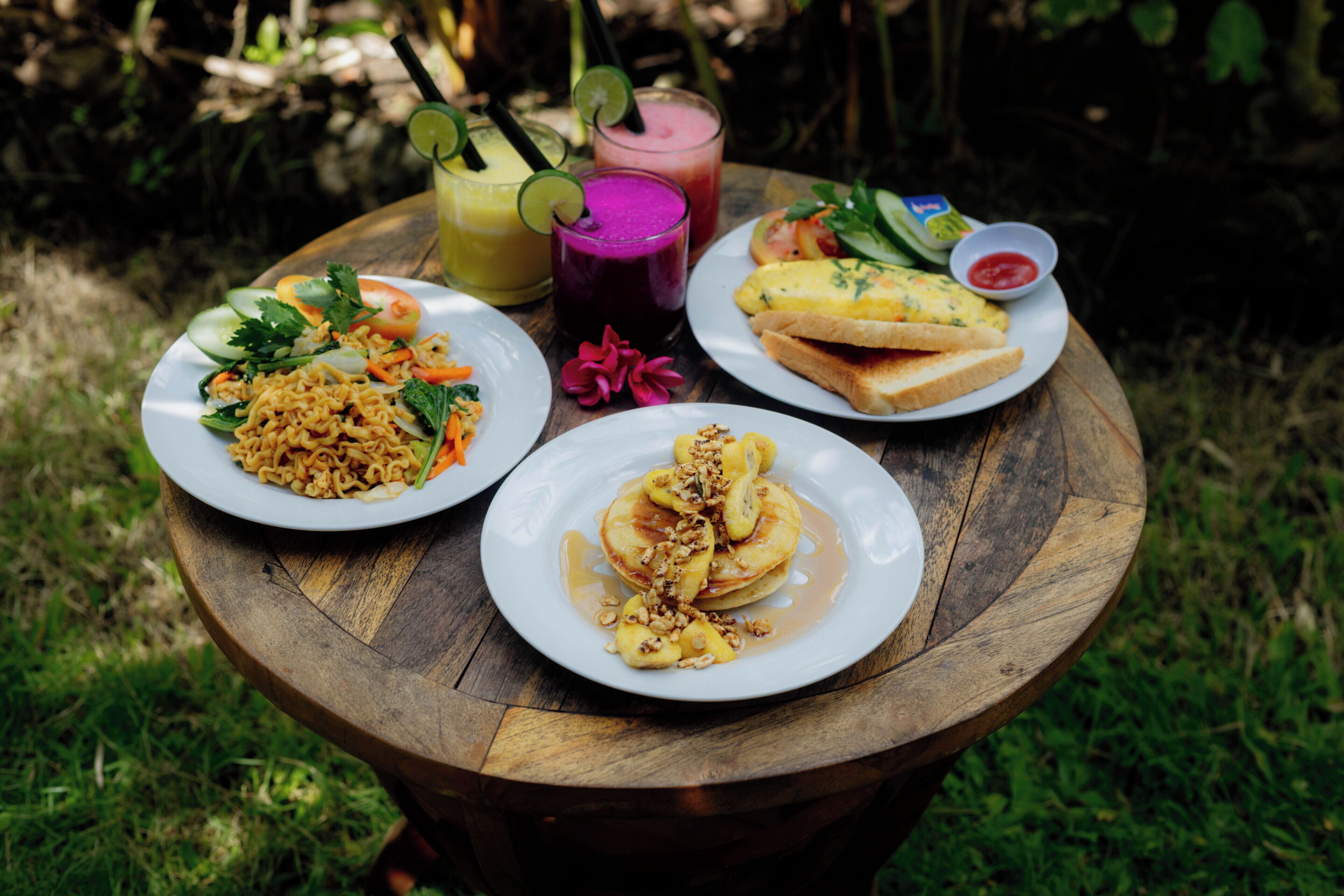 A wooden table with four plates of food, two drinks, and a small bowl of sauce.