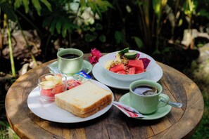 Une table en bois sur laquelle se trouvent une assiette de toasts, un verre de jus de fruits, une tasse de café et un bol de fruits.