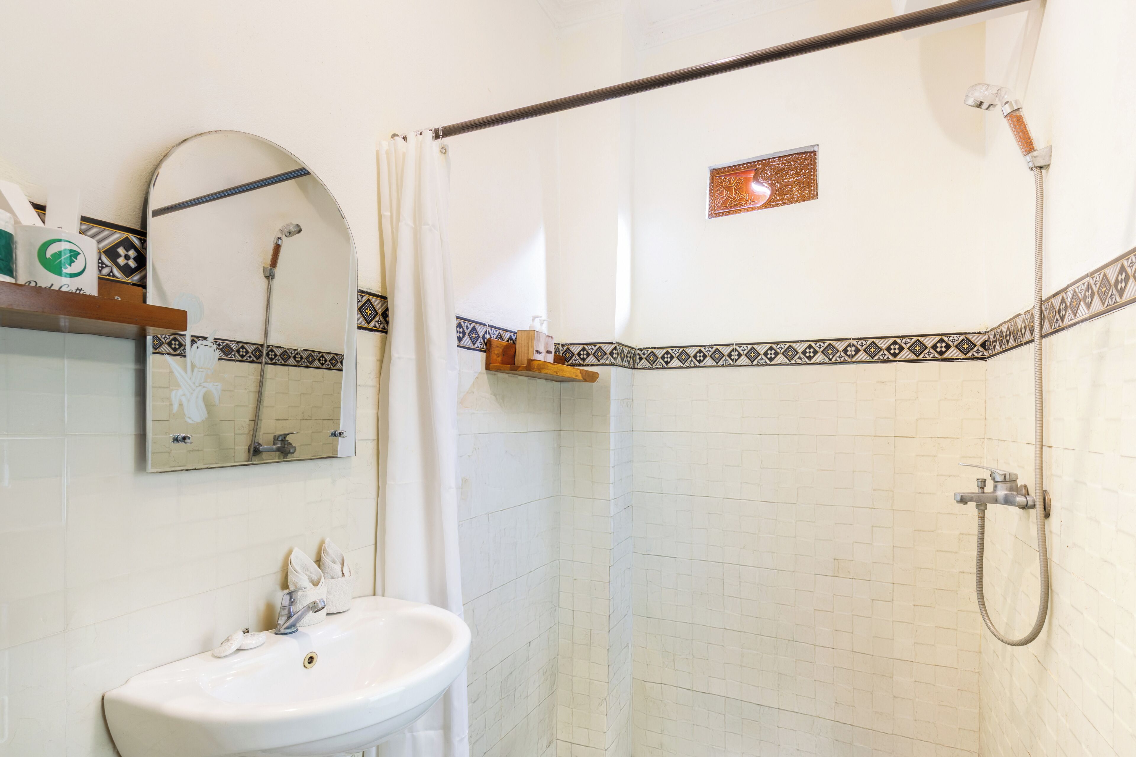 Un baño con lavamanos blanco, un espejo, ducha con cabezal de ducha de mano y un perchero para toallas.