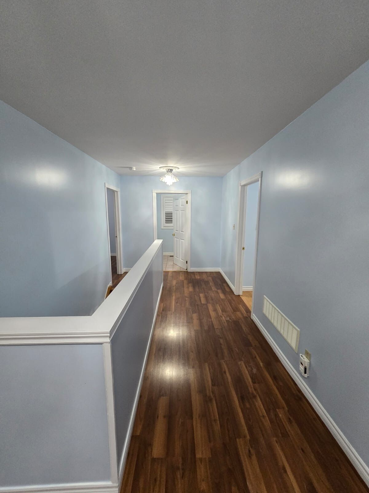A hallway with light blue walls and wooden flooring, leading to a door at the end.