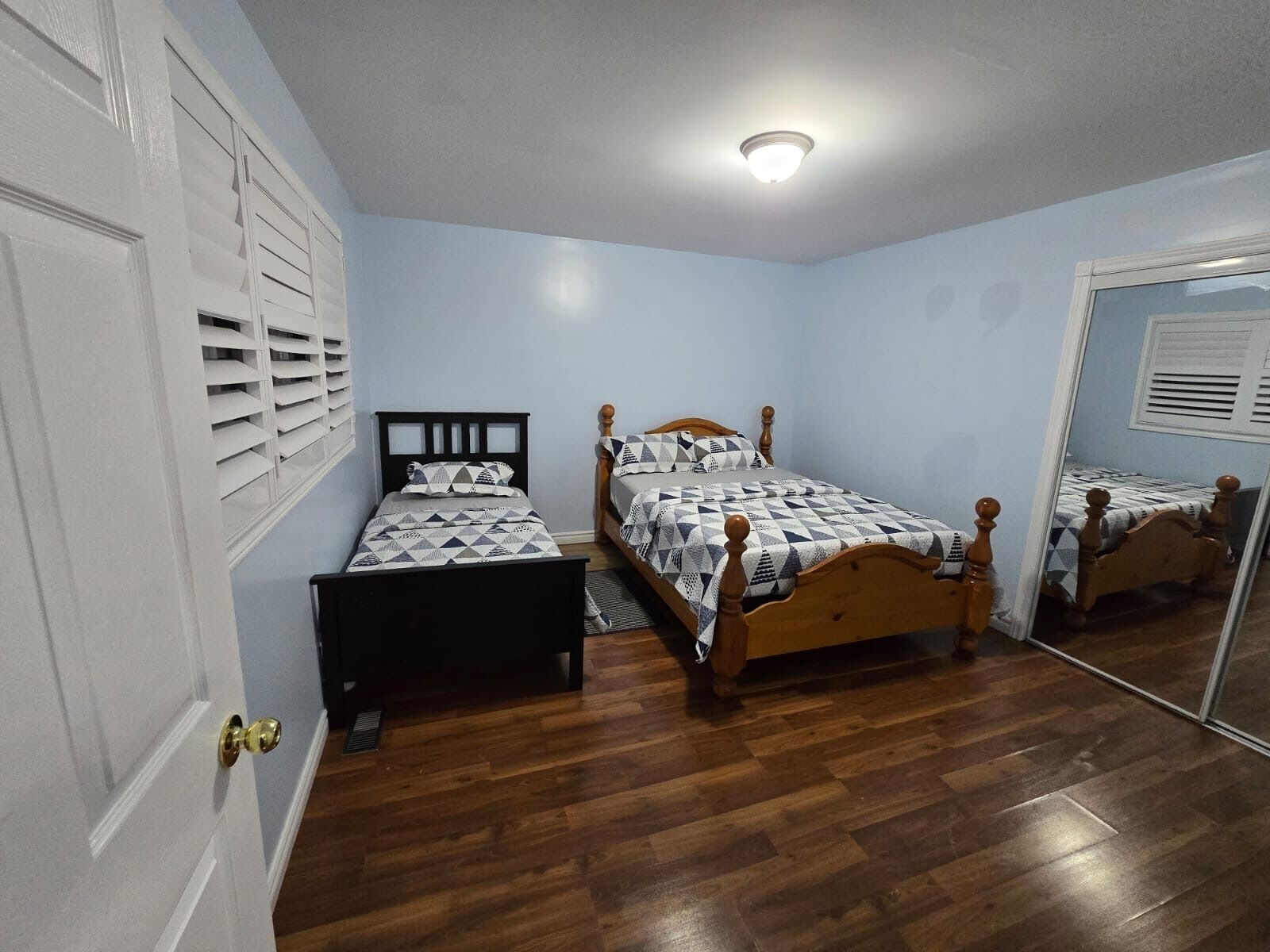 A bedroom with two beds, wooden flooring, and a ceiling light.