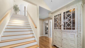 A staircase with wooden steps and a white handrail, leading to a room with a wooden floor and a white cabinet with glass doors. - Harbor Haven-Ocean Views, Steps to Beach + Dining (Santa Cruz)