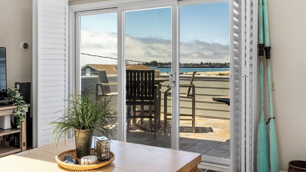 A room with a sliding glass door leading to a patio with outdoor furniture and a view of a beach. - Harbor Haven-Ocean Views, Steps to Beach + Dining (Santa Cruz)