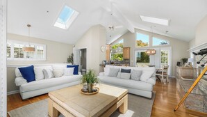 A spacious living room with a large white sofa, a wooden coffee table, and a view of the kitchen through an open doorway. - Harbor Haven-Ocean Views, Steps to Beach + Dining (Santa Cruz)