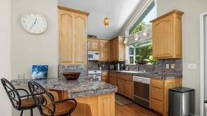 A kitchen with wooden cabinets, a granite countertop, a dishwasher, and a trash can. - Harbor Haven-Ocean Views, Steps to Beach + Dining (Santa Cruz)