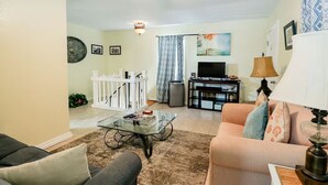 Un salon avec une table basse en verre, un canapé, un meuble pour la télévision et une lampe.