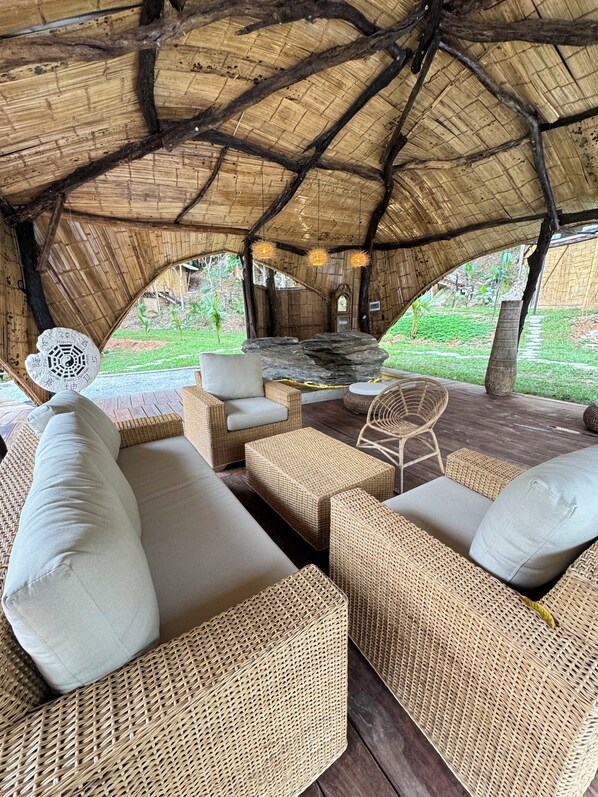 A thatched-roof outdoor seating area with wicker furniture and a stone table.