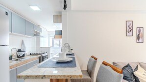 A modern kitchen with a central island, grey cabinets, and a dining area with a grey sofa and blue placemats. - Apartment in Santos, 2 bedrooms, brand new, decorated, pet friendly - Aloha 181. (Santos)
