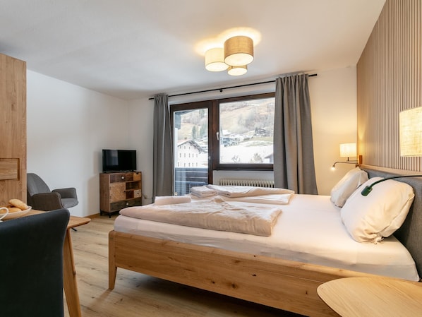 Une chambre avec un lit en bois, une télévision, un bureau et une fenêtre avec des rideaux.