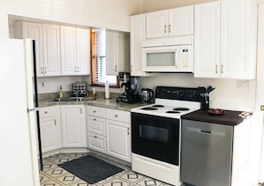 Une cuisine de taille réduite, avec des meubles blancs, un four à micro-ondes, une cuisinière et un réfrigérateur.