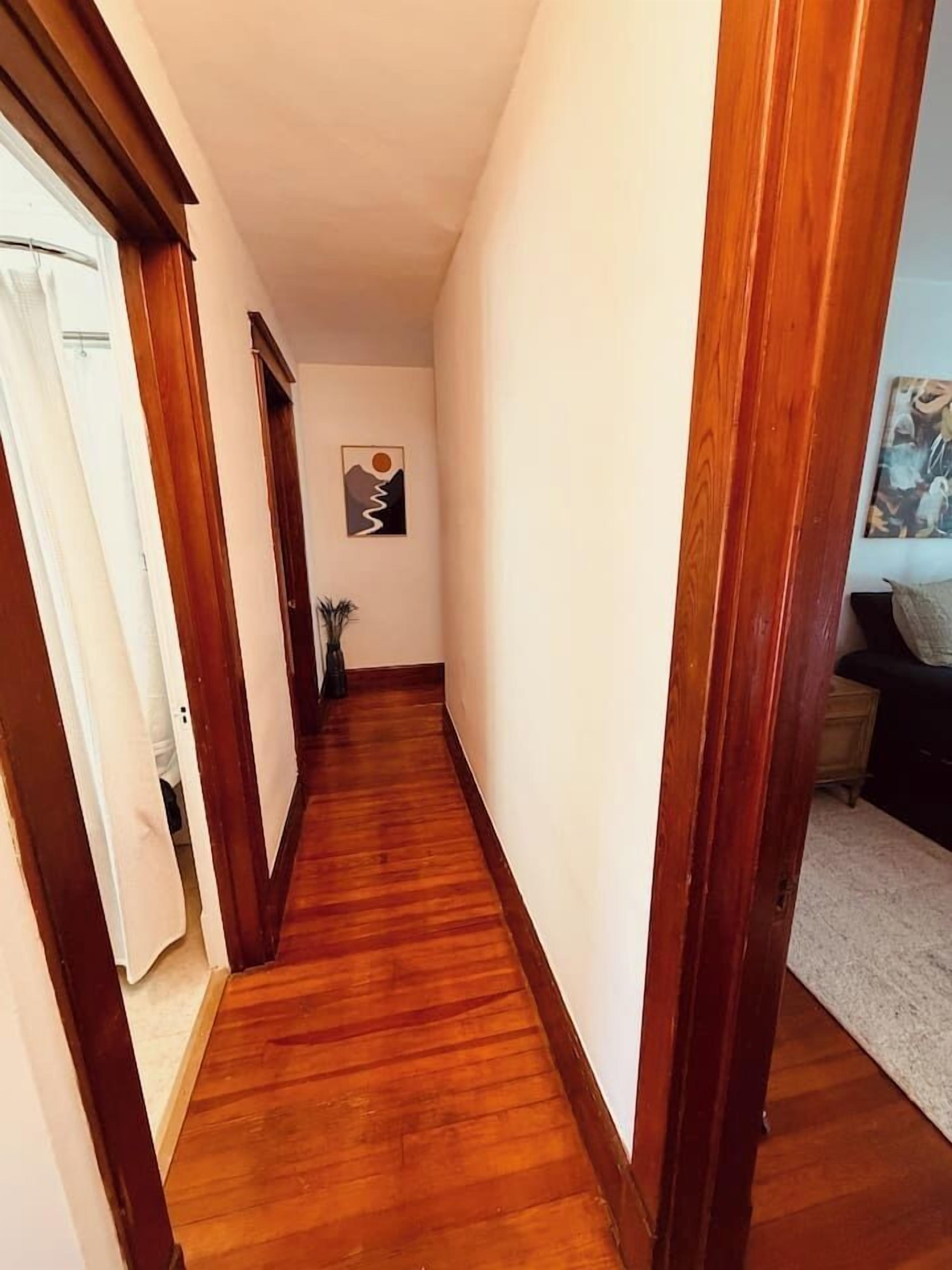 A narrow hallway with wooden flooring and white walls.