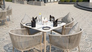 A dining area with a round table set for four, surrounded by wicker chairs with cushions. - JBM RESORTS & WATER PARK (Abohar)
