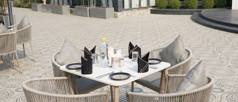 A dining area with a round table set for four, surrounded by wicker chairs with cushions.