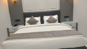 A neatly made bed with a quilted headboard, two bedside tables with lamps, and a water bottle on one of the tables. - JBM RESORTS & WATER PARK (Abohar)