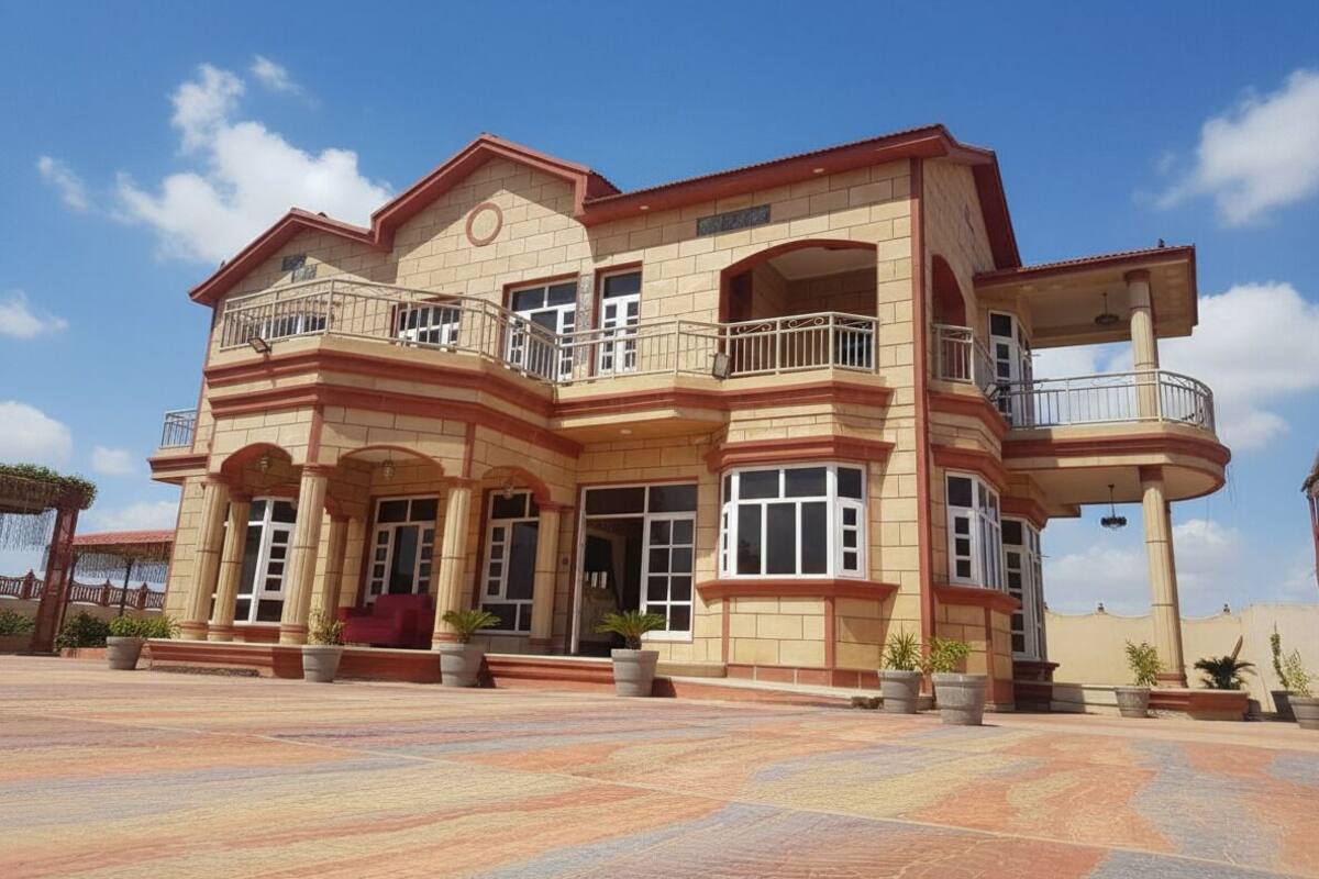 A large, multi-story building with a symmetrical facade, multiple balconies, and a spacious entrance area with potted plants.