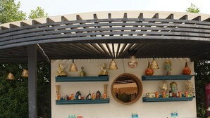 An outdoor bar area with a pergola, wicker chairs, a patterned floor, and shelves with decorative items. - JBM RESORTS & WATER PARK (Abohar)