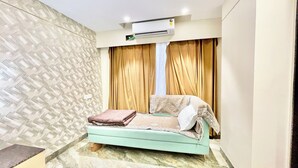 A small, well-lit room with a bed, an air conditioning unit, and patterned walls. - Premium Hotel M Shri near Mahakal Temple (Ujjain)