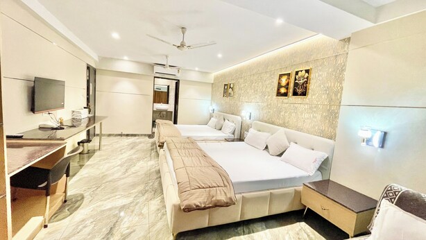 A modern hotel room with two beds, a desk, a television, and a bathroom visible through an open door. - Premium Hotel M Shri near Mahakal Temple (Ujjain)